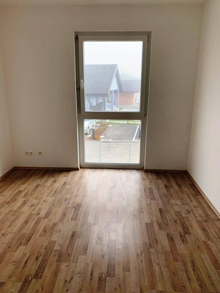 Schlafzimmer mit Laminatboden und einem großen Fenster, das viel Tageslicht hereinlässt.