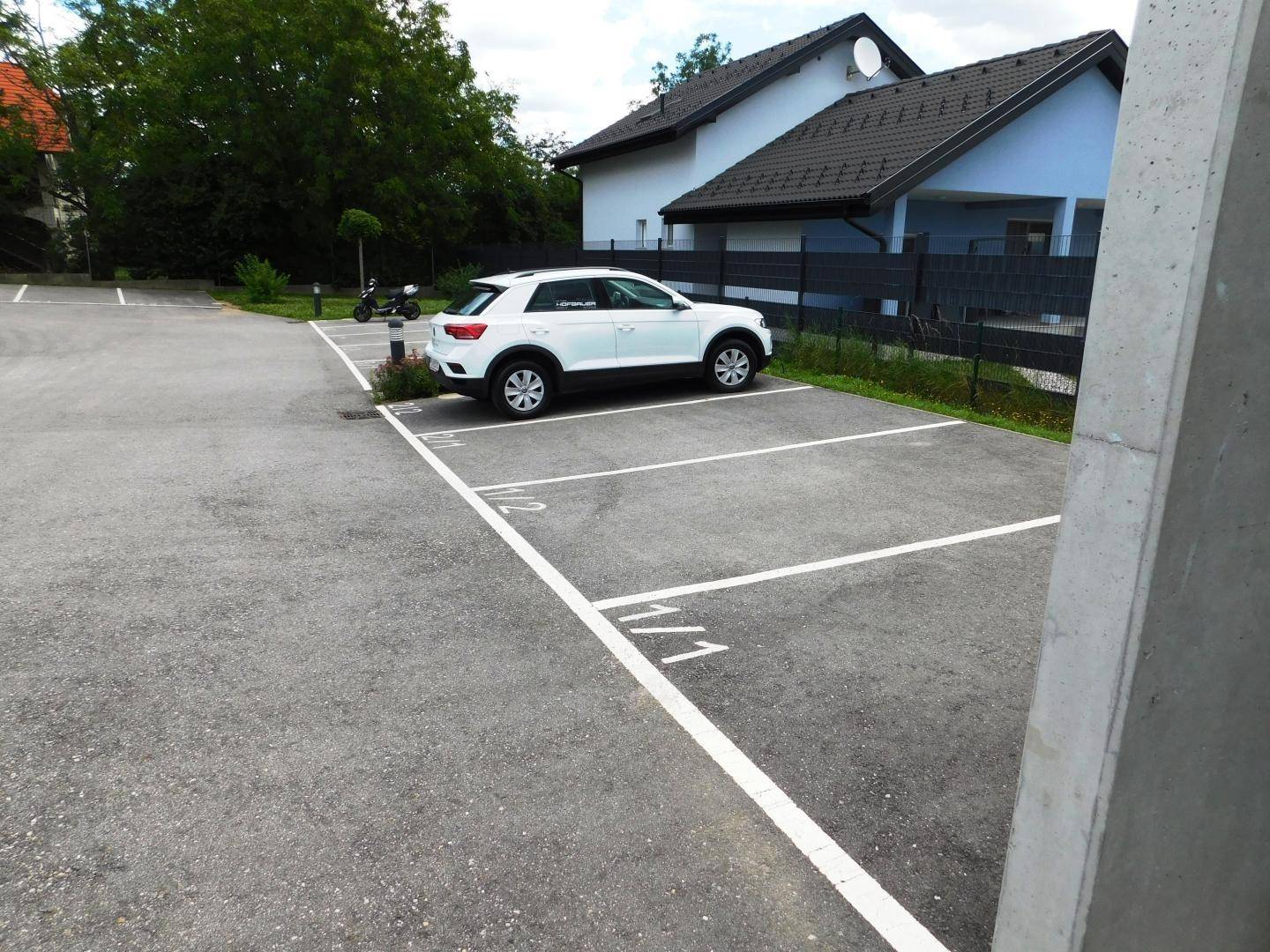 Außenparkplätze mit markierten Stellflächen vor einem Wohngebäude, ein Auto ist geparkt.