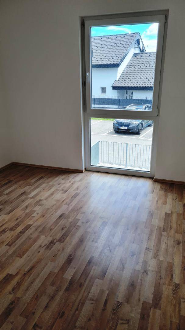Helles Schlafzimmer mit Laminatboden und einem Fenster mit Blick auf den Parkplatz.