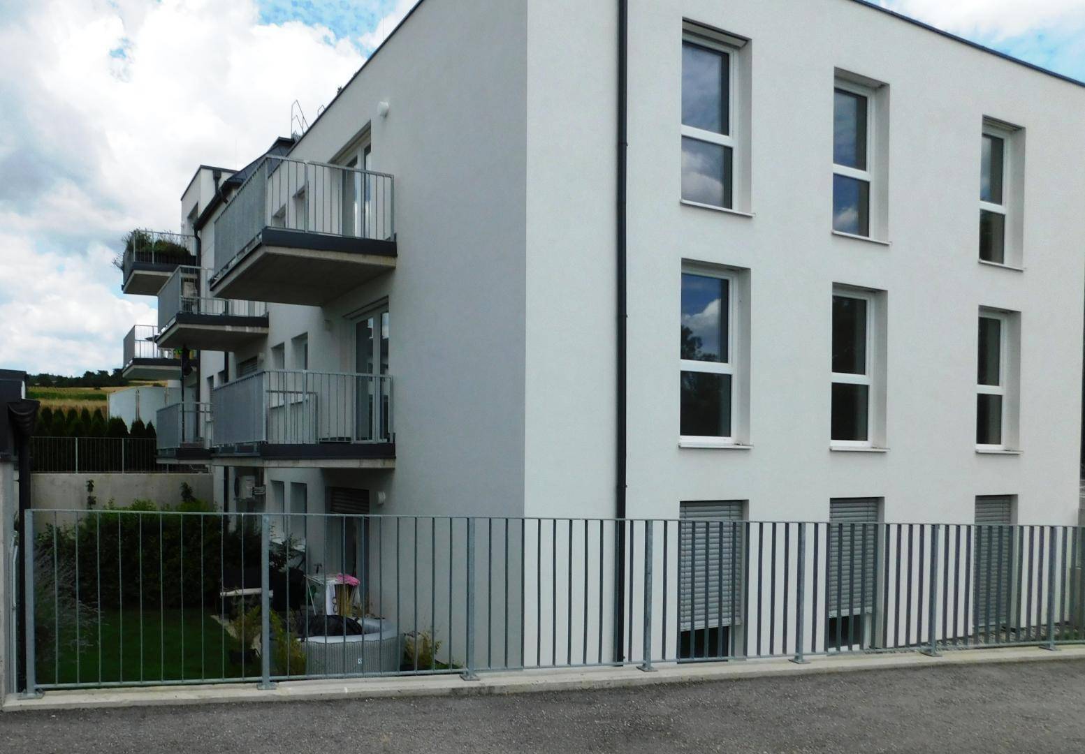 Ansicht eines modernen Wohngebäudes mit Balkonen und großen Fenstern im Erdgeschossbereich.