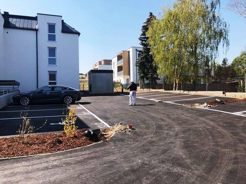Außenansicht eines modernen Neubaus mit einem großen, asphaltierten Parkplatz und Bäumen.
