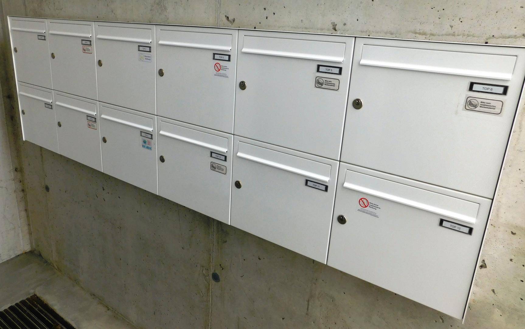 Reihe von weißen Briefkästen an einer Betonwand im Eingangsbereich des Gebäudes.
