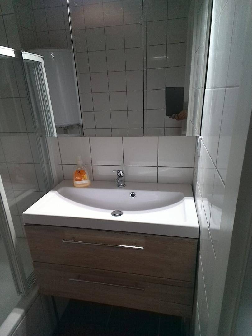 Modernes Badezimmer mit Einzelwaschbecken, Spiegelschrank und weißen Fliesen an den Wänden.