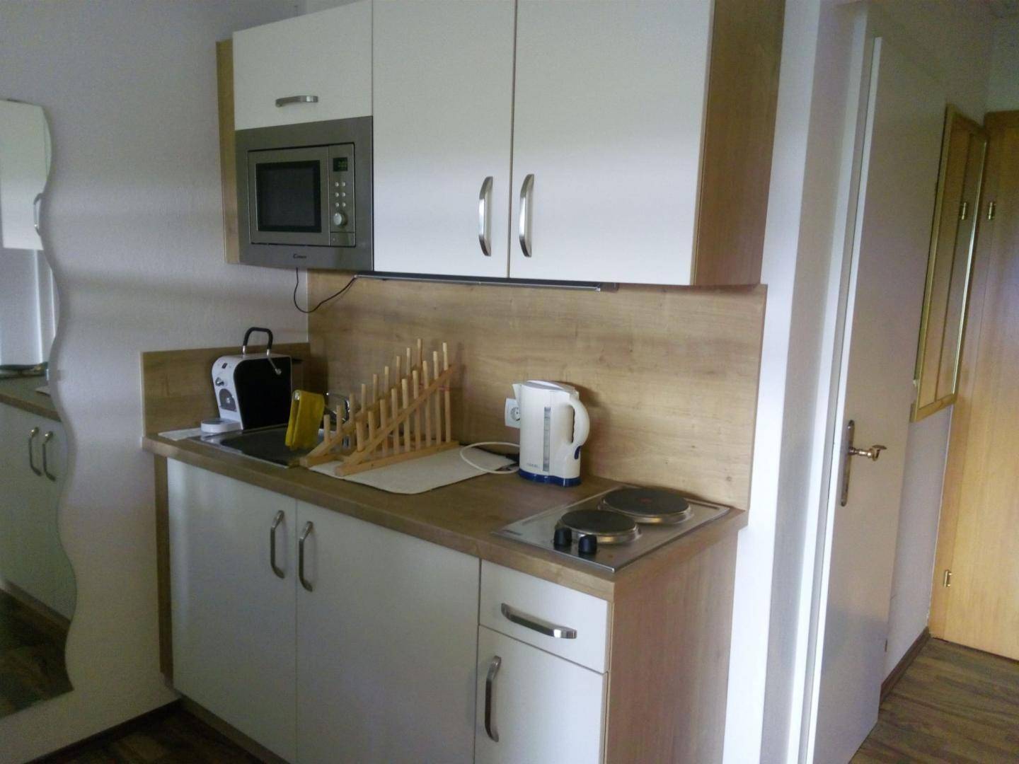 Kleine Küchenzeile mit weißen Schränken, Holzarbeitsplatte und integrierter Mikrowelle.