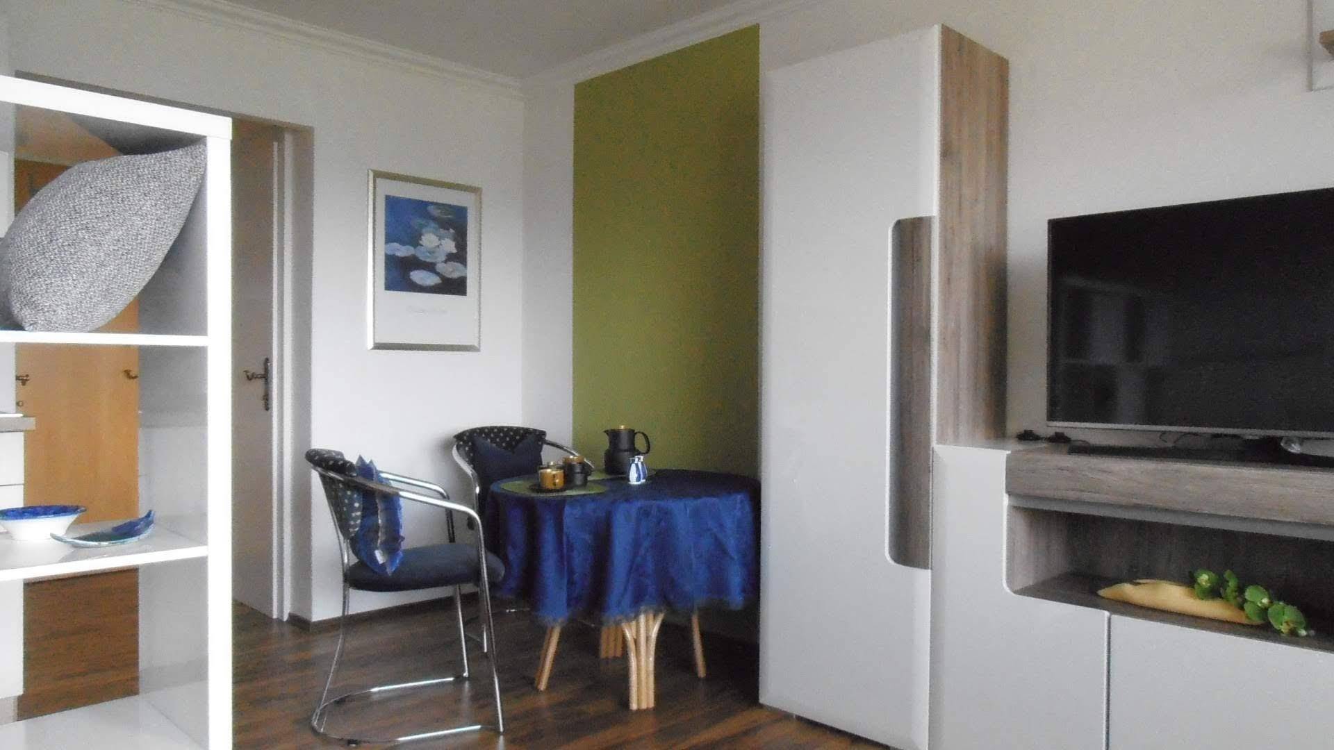 Gemütlicher Wohn-Essbereich mit Holzboden, einem kleinen Esstisch und einer grünen Akzentwand.