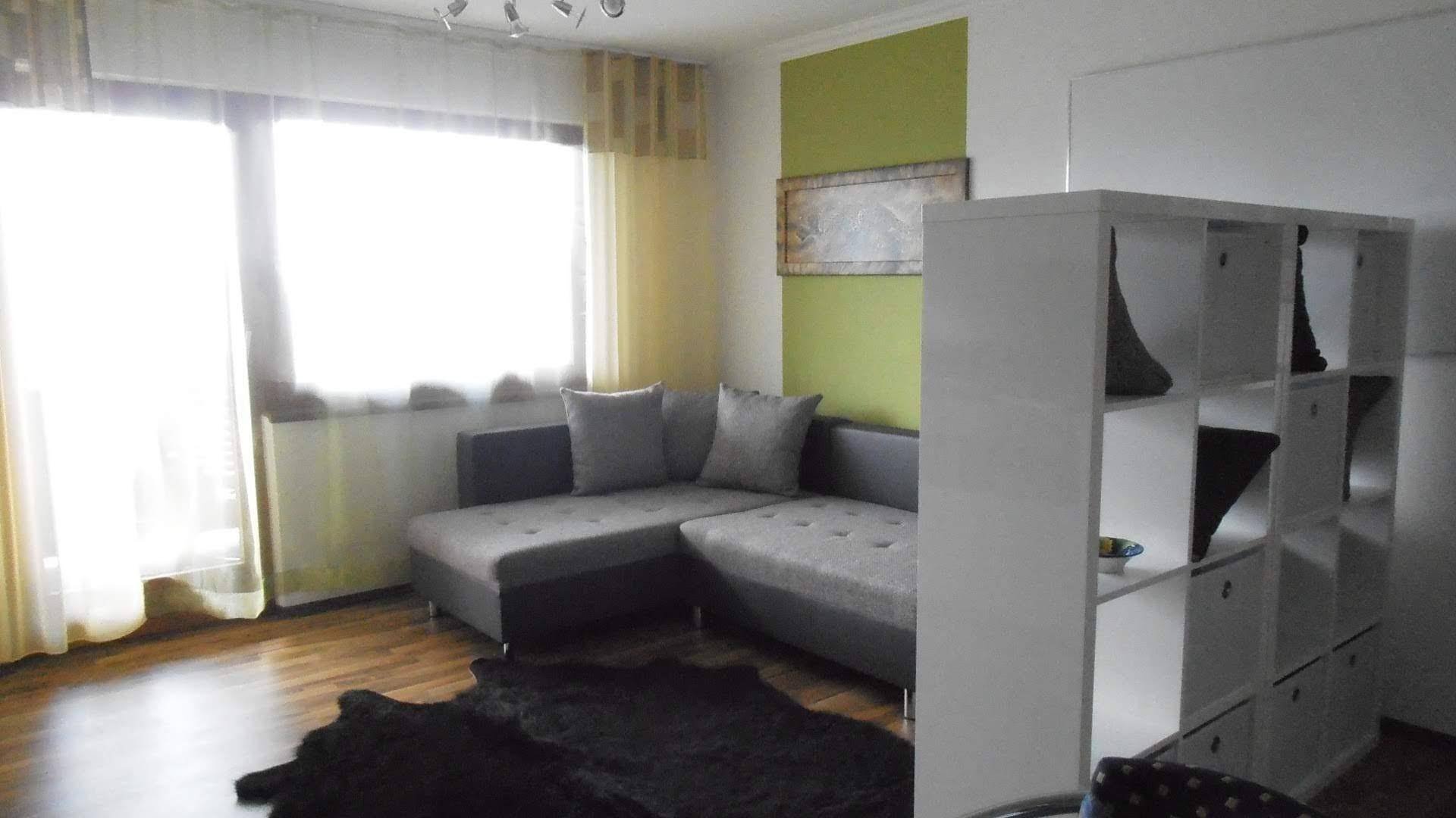 Helles Wohnzimmer mit grauem Ecksofa, Holzboden und großen Fenstern für viel Tageslicht.