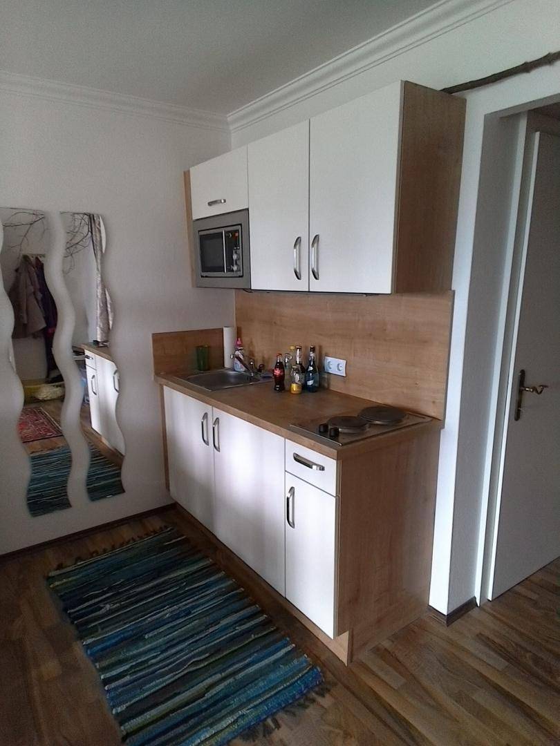 Kleine Küchenzeile mit weißen Schränken, Holzarbeitsplatte und einem bunten Teppich auf dem Boden.