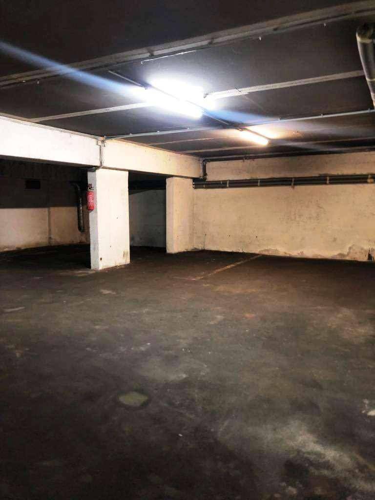 Helle Tiefgarage mit Betonwänden und -boden, ausgestattet mit Deckenbeleuchtung.