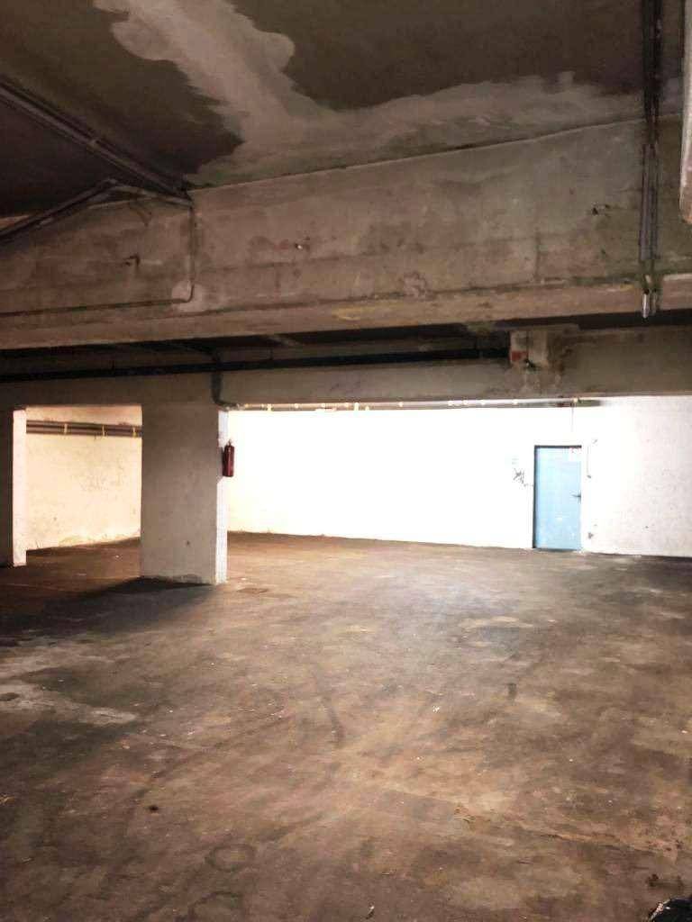Große, leere Tiefgarage mit Betonstützen und einer blauen Tür im Hintergrund.