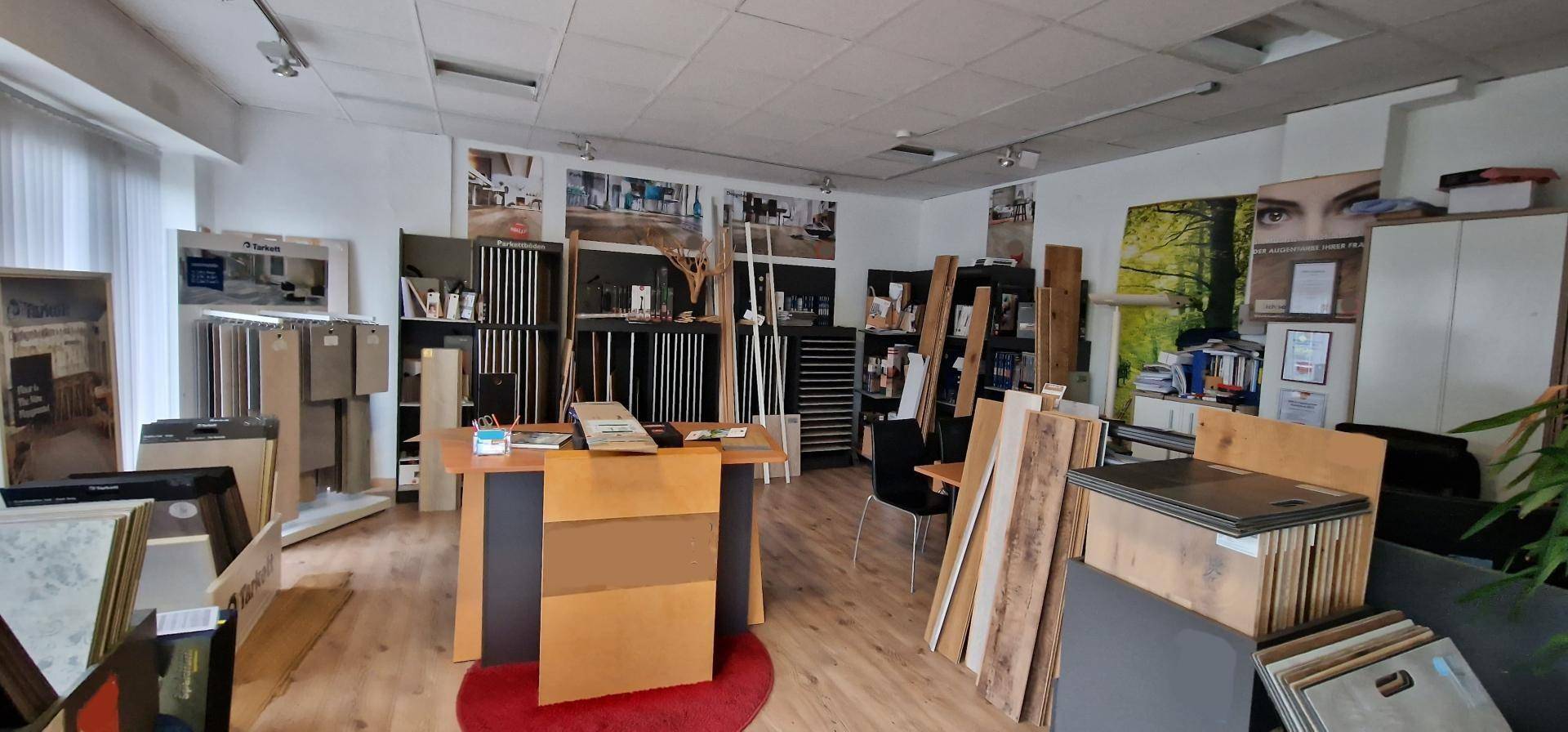 Geräumiger Ausstellungsraum mit verschiedenen Bodenbelagsmustern und einem zentralen Schreibtischbereich.