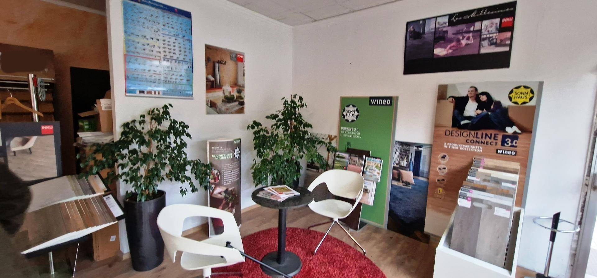 Helle Ecke eines Ausstellungsraums mit modernen Stühlen, einem runden Tisch und dekorativen Pflanzen.