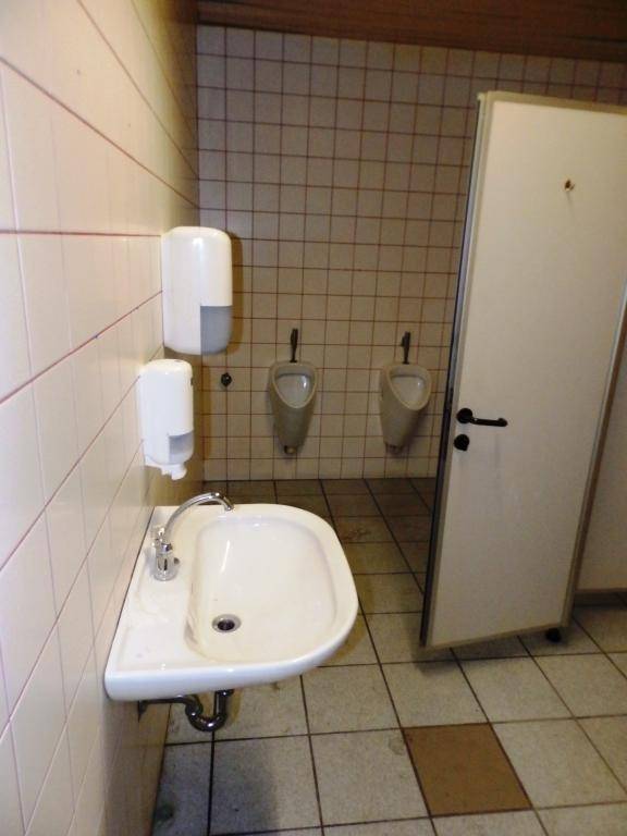 Ein öffentlicher Waschraum mit Fliesen an Wänden und Boden, ausgestattet mit Waschbecken und Urinalen.