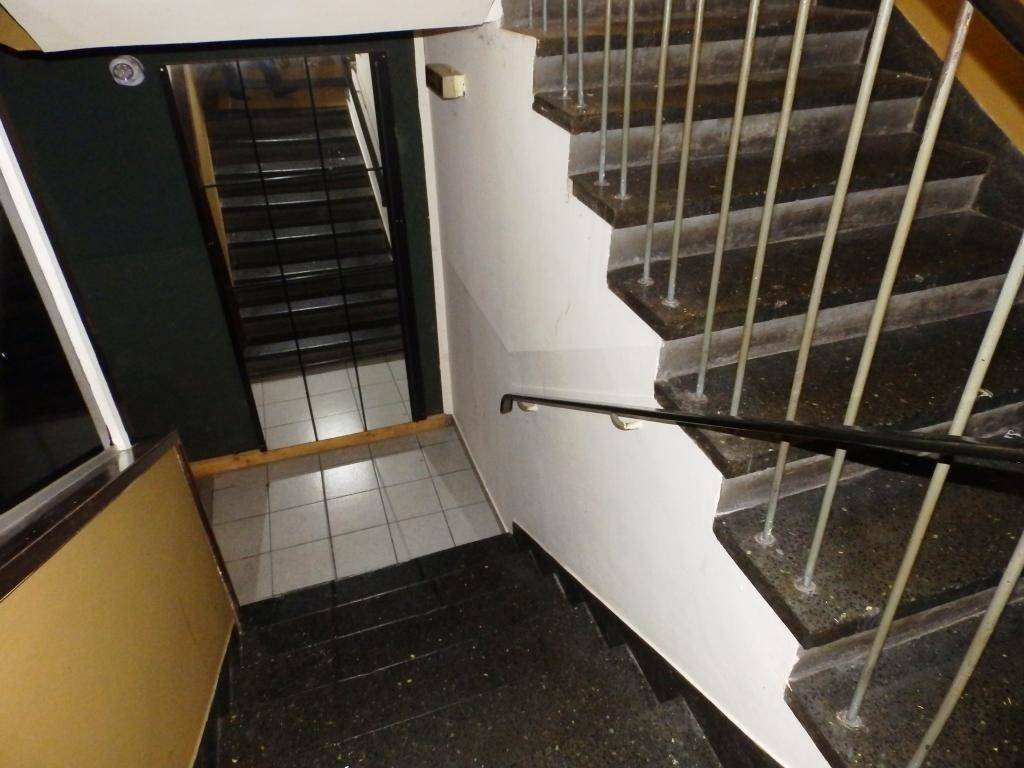 Ein Treppenhaus mit Terrazzostufen, Metallgeländer und Fliesenboden im Eingangsbereich.