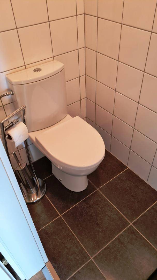 Separates WC mit weißer Toilette und braunen Bodenfliesen.