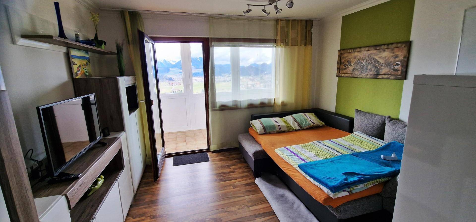 Gemütlicher Wohnbereich mit Schlafsofa, Fernseher und Zugang zu einem Balkon mit Bergblick.