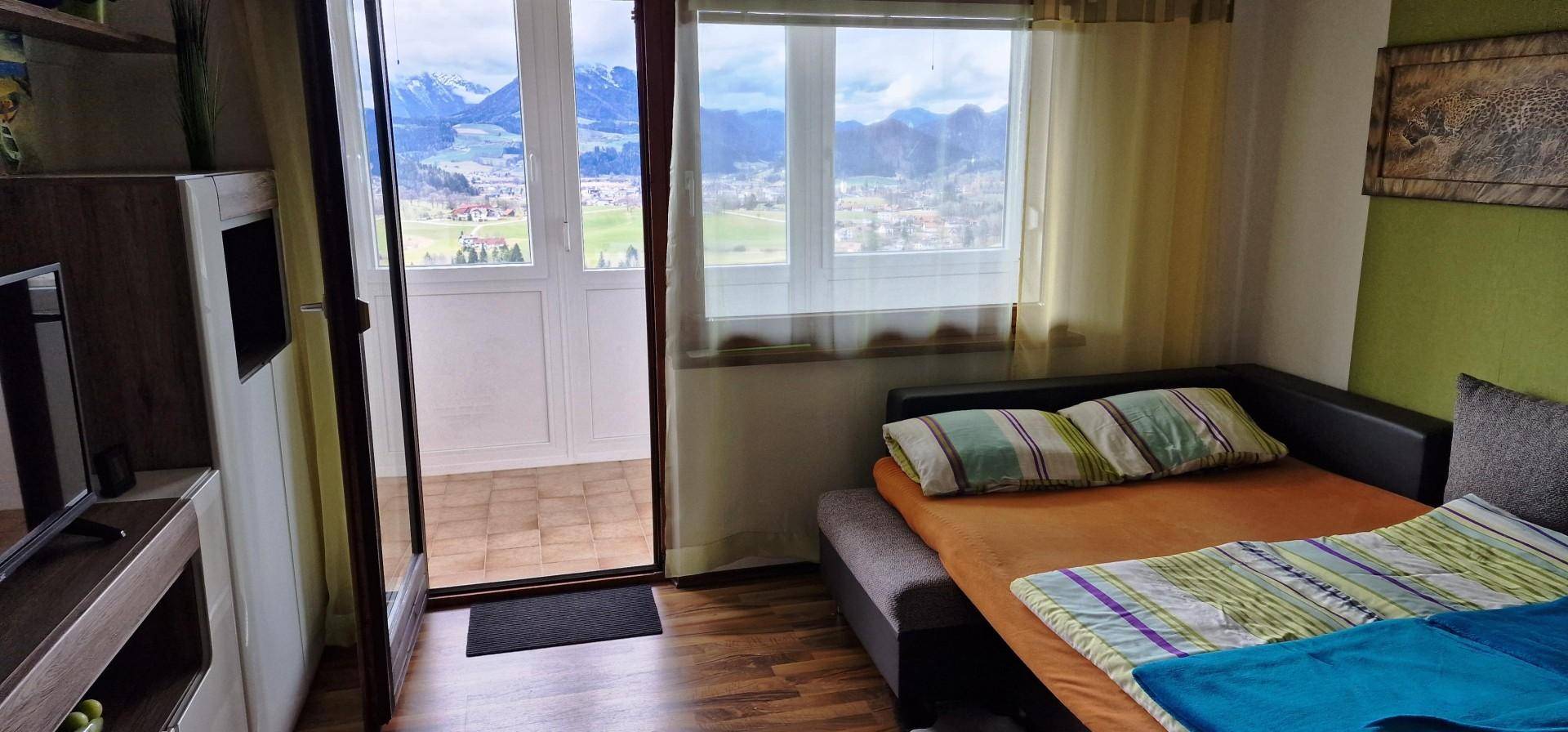 Heller Wohnraum mit Schlafgelegenheit und direktem Zugang zu einem Balkon mit Panoramablick.