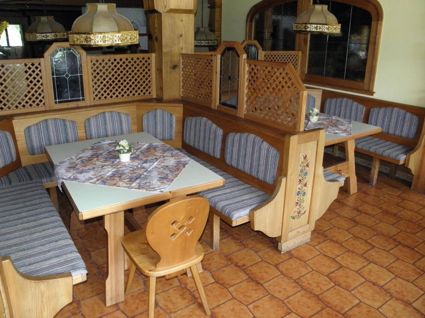 Nahaufnahme des Essbereichs mit traditionellen Holzmöbeln, gepolsterten Bänken und gemusterten Tischdecken.