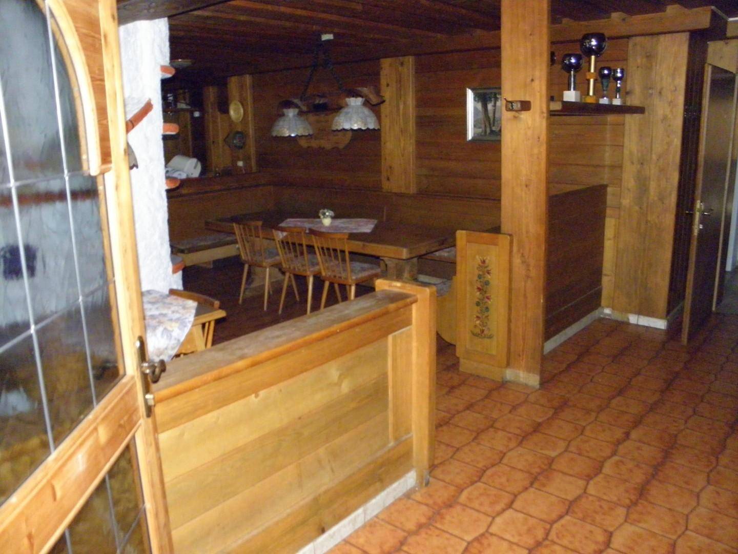 Traditioneller Essbereich im alpinen Stil mit Holztisch, Eckbank und Kachelofen im Hintergrund.