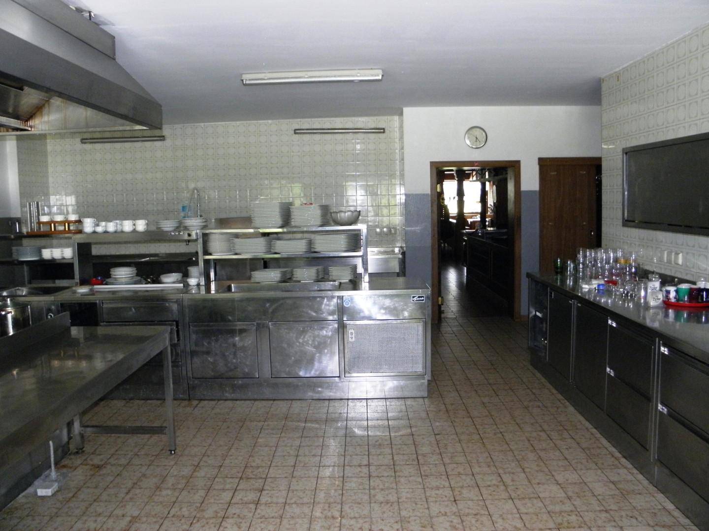 Professionelle Küche mit Edelstahlmöbeln, Fliesenboden und Geschirrregalen, bereit für den Gastronomiebetrieb.