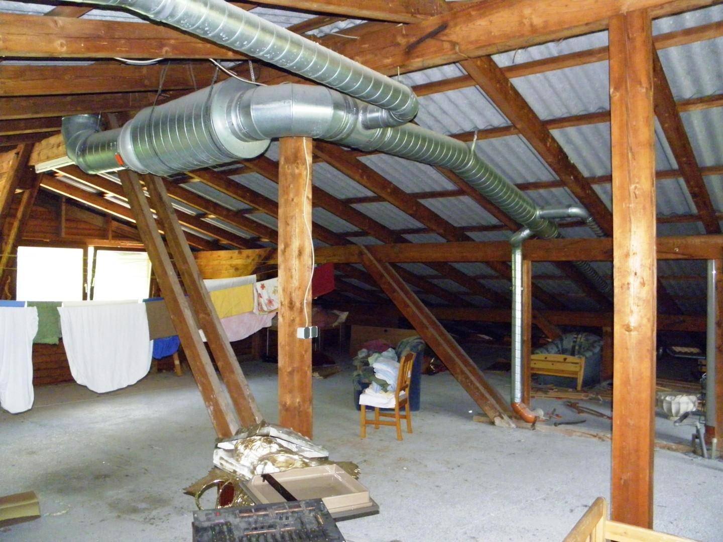 Unausgebauter Dachboden mit sichtbaren Holzbalken, Lüftungsrohren und Wäsche zum Trocknen.