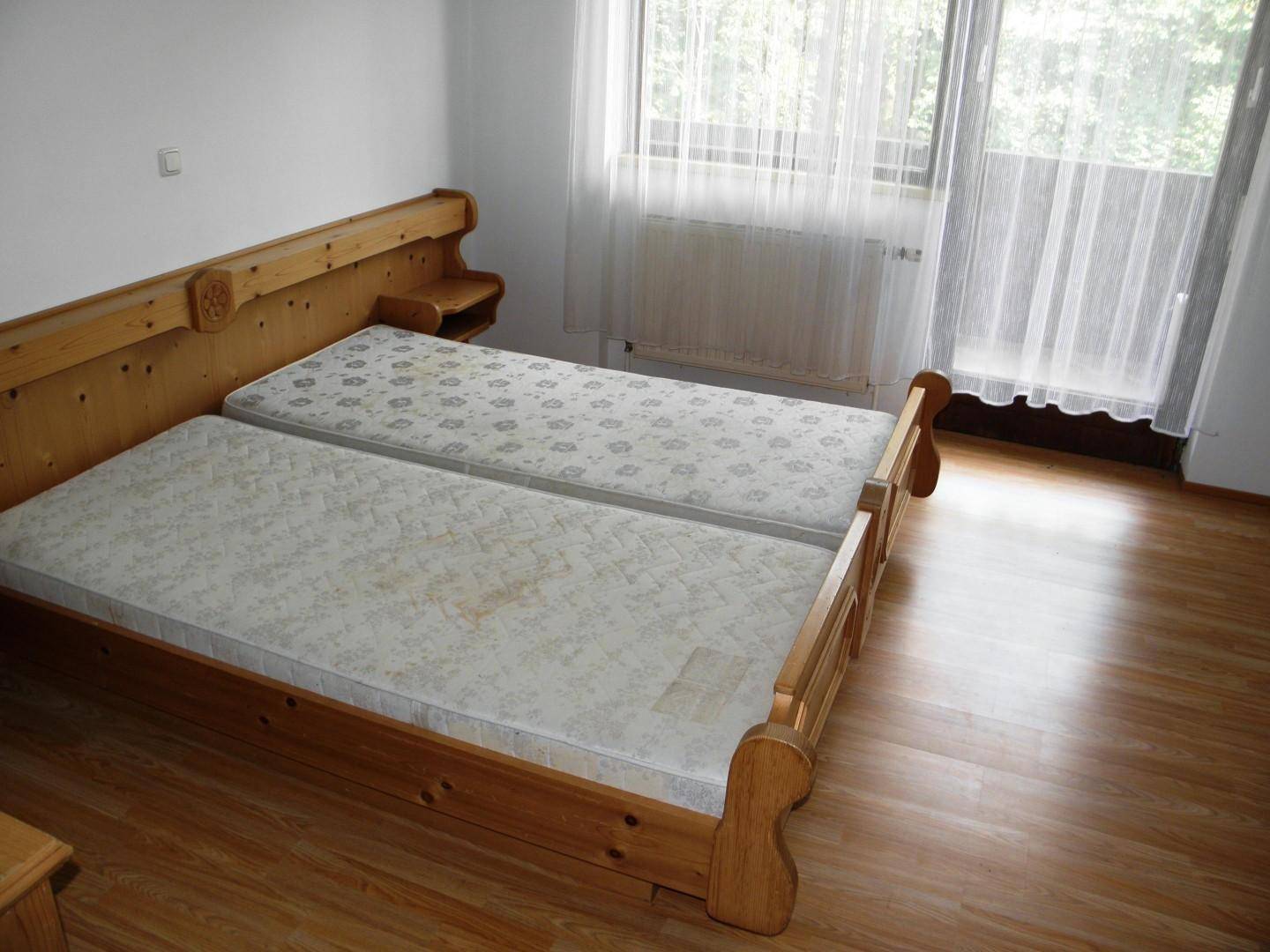 Schlafzimmer mit zwei Einzelbetten, Holzmöbeln und Zugang zu einem Balkon durch große Fenster.