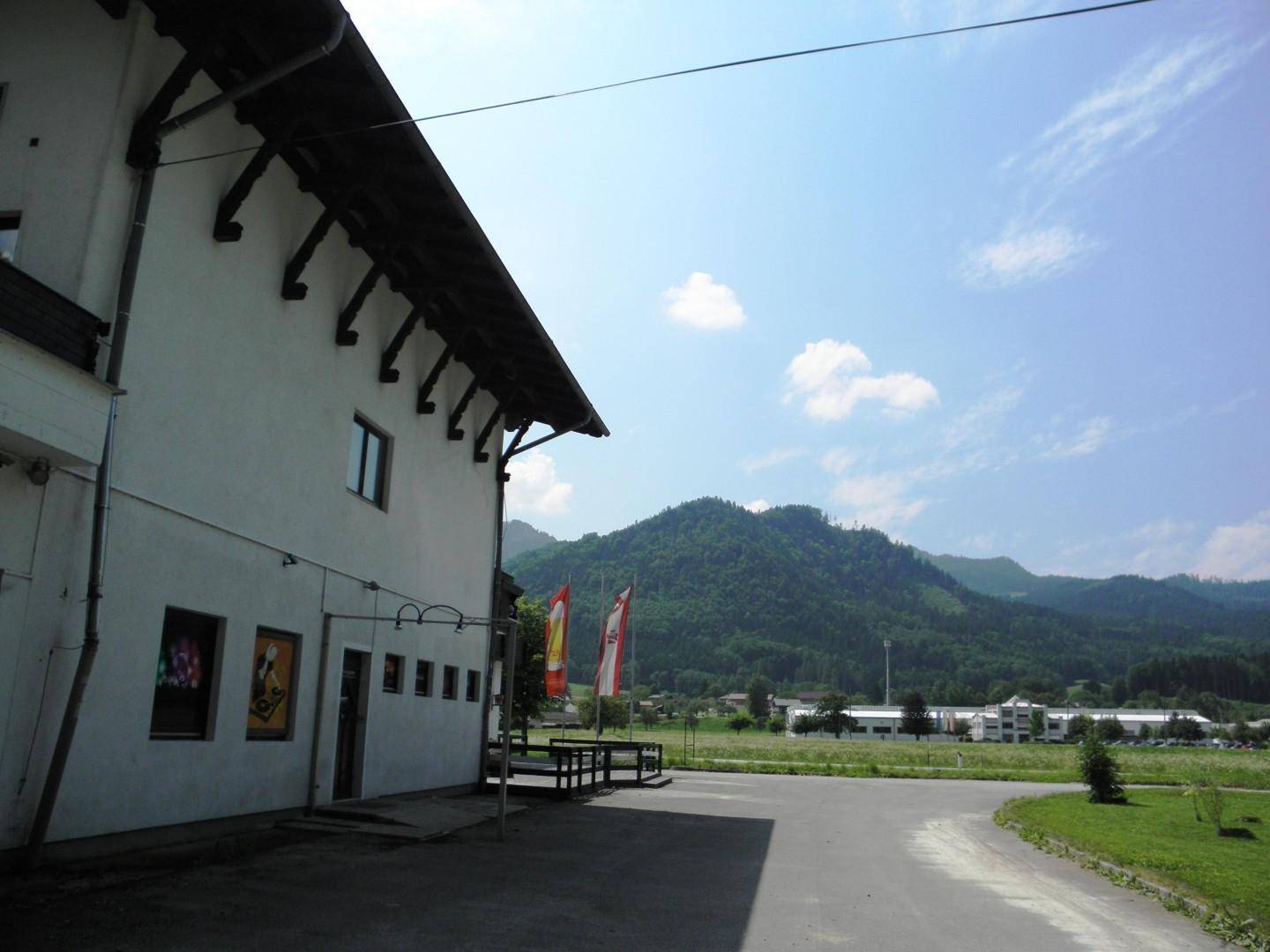 Seitenansicht des Gebäudes mit Blick auf die weite Landschaft und die bewaldeten Berge im Hintergrund.