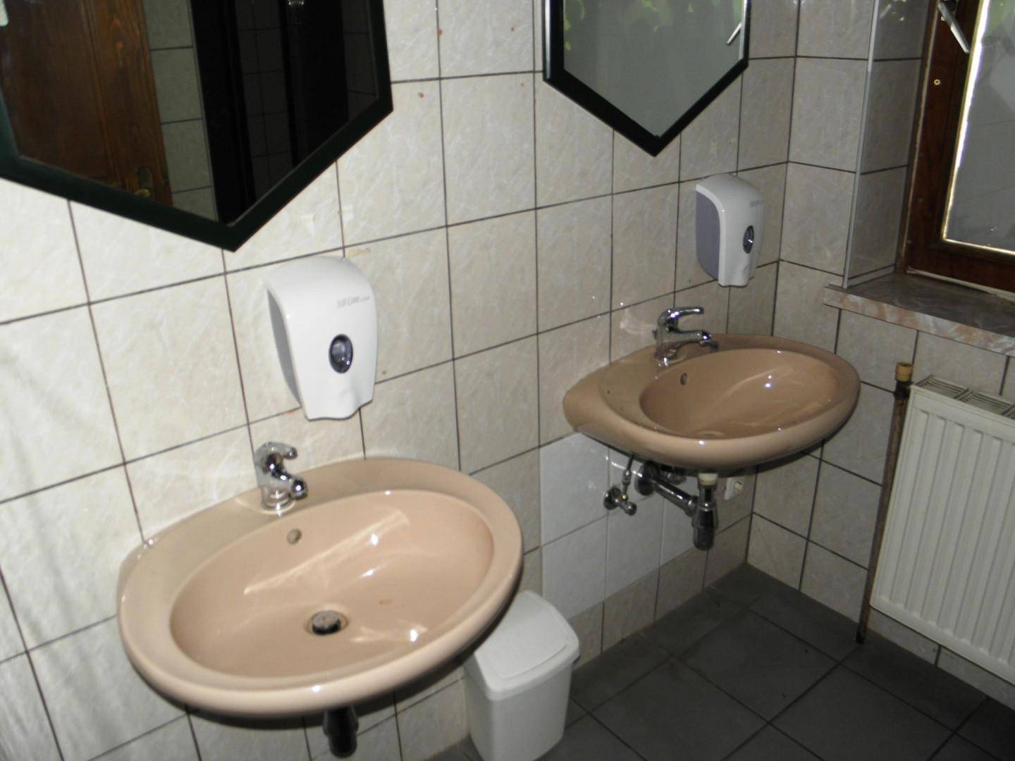 Waschraum mit zwei Waschbecken, Spiegeln, Fliesenwänden und einem Fenster für Tageslicht.