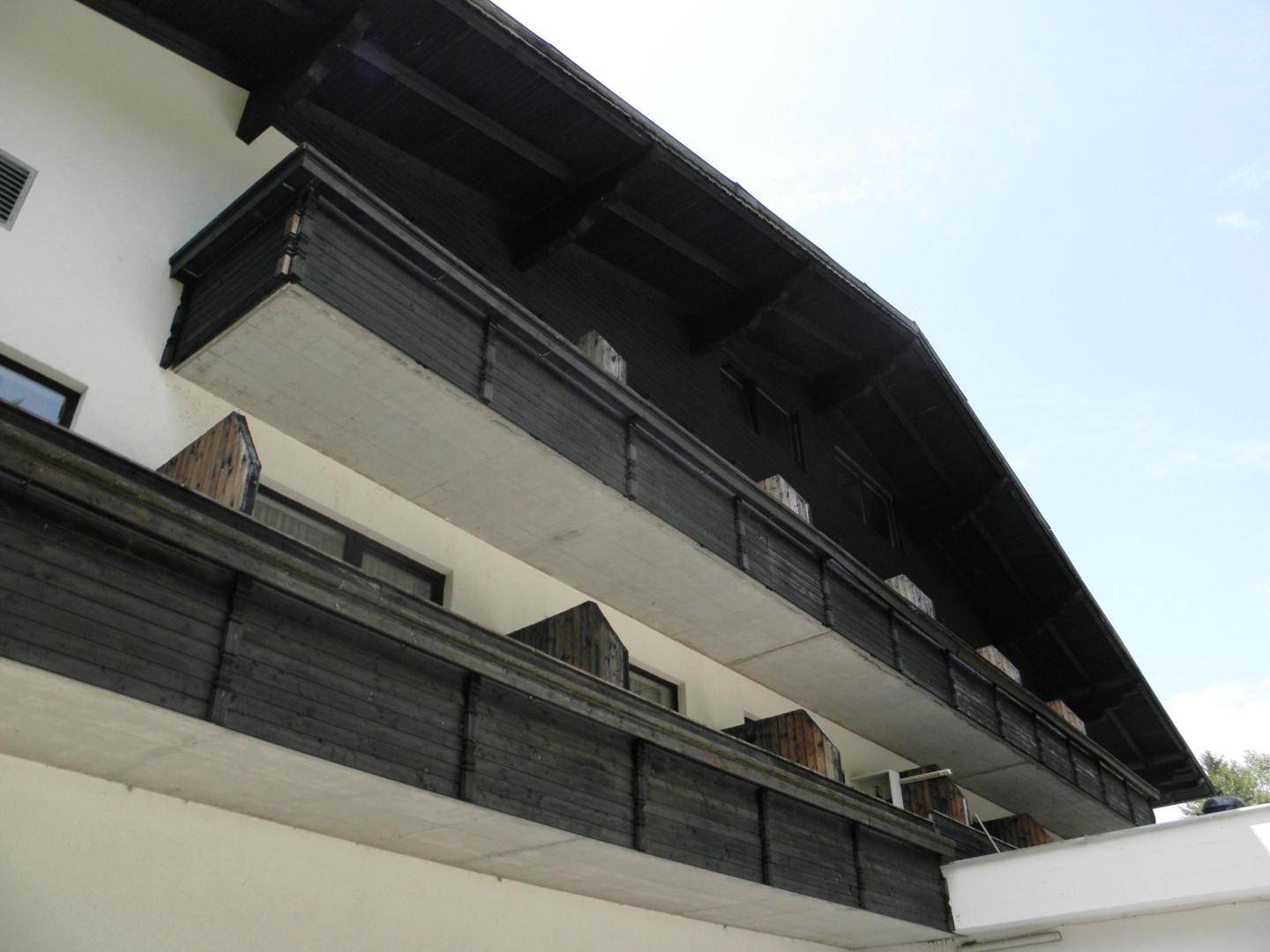 Nahaufnahme der dunklen Holzbalustraden und Betonplatten der Balkone an der Fassade des Gebäudes.