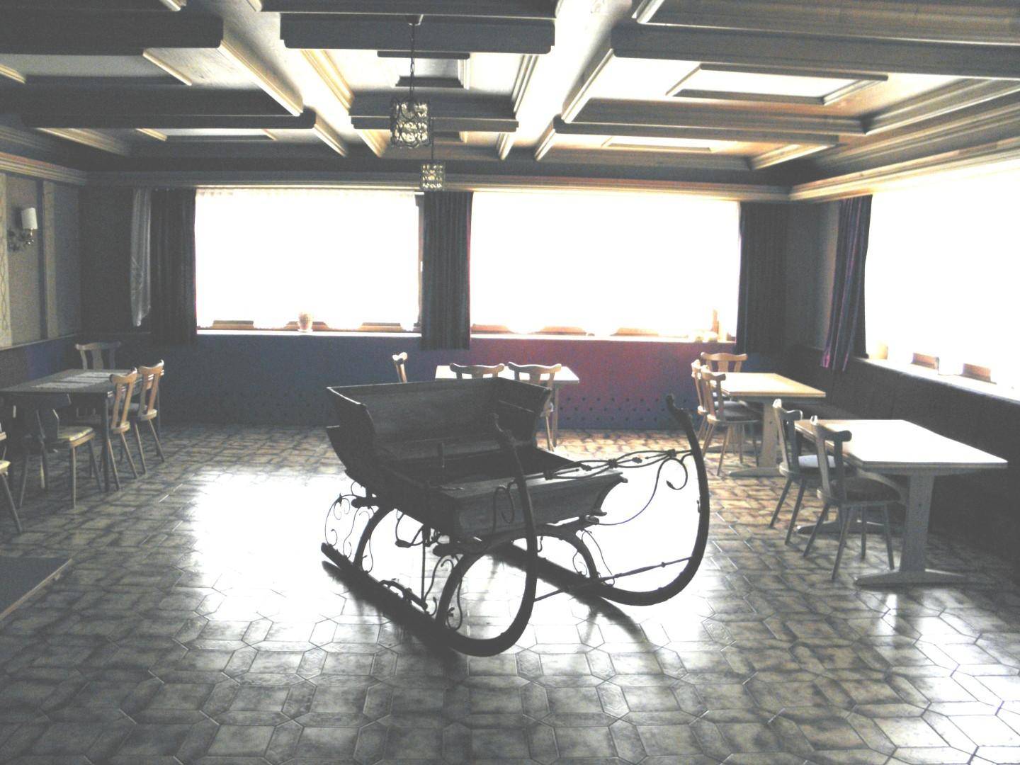 Geräumiger Speisesaal mit Holztäfelung an der Decke, großen Fenstern und einem dekorativen Schlitten in der Mitte.