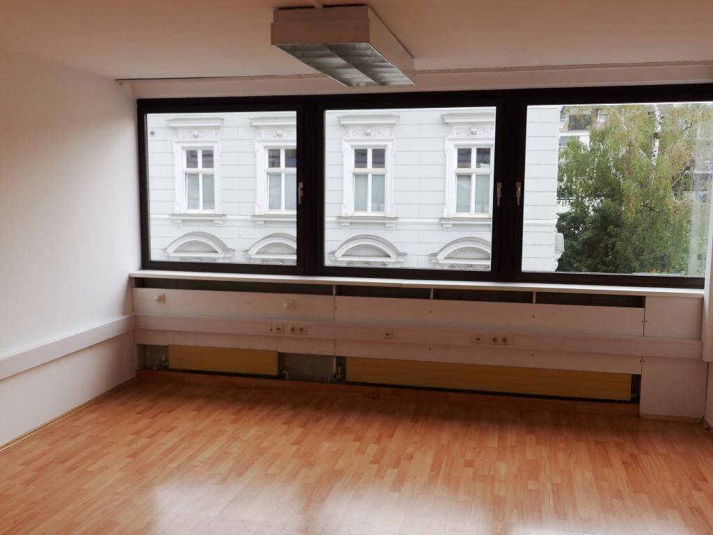 Heller Büroraum mit drei Fenstern und Blick auf die gegenüberliegenden Gebäude.