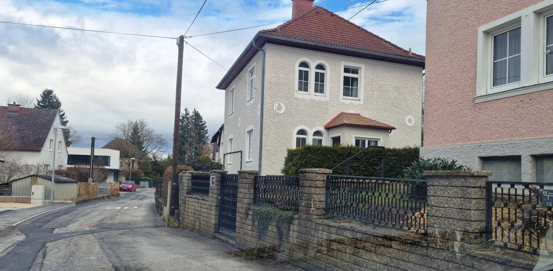 Seitenansicht des Wohnhauses mit klassischer Architektur, Satteldach und umzäuntem Vorgartenbereich.