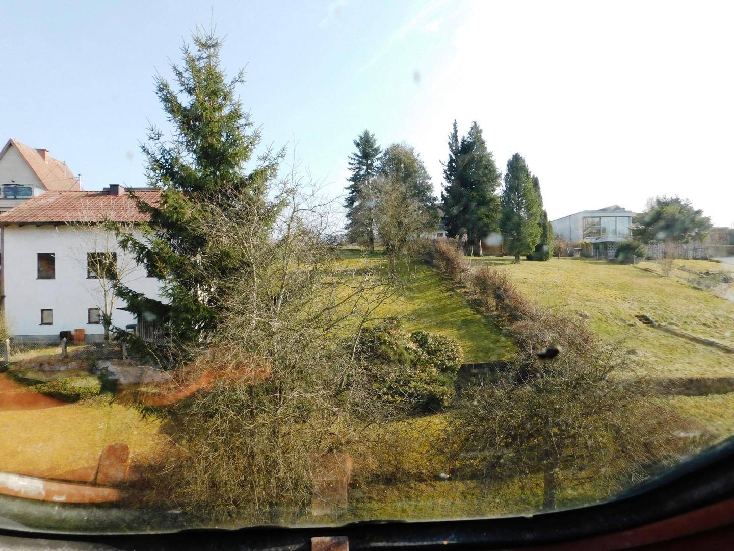 Blick auf ein Wohnhaus und eine grüne Hügellandschaft mit Bäumen unter blauem Himmel.