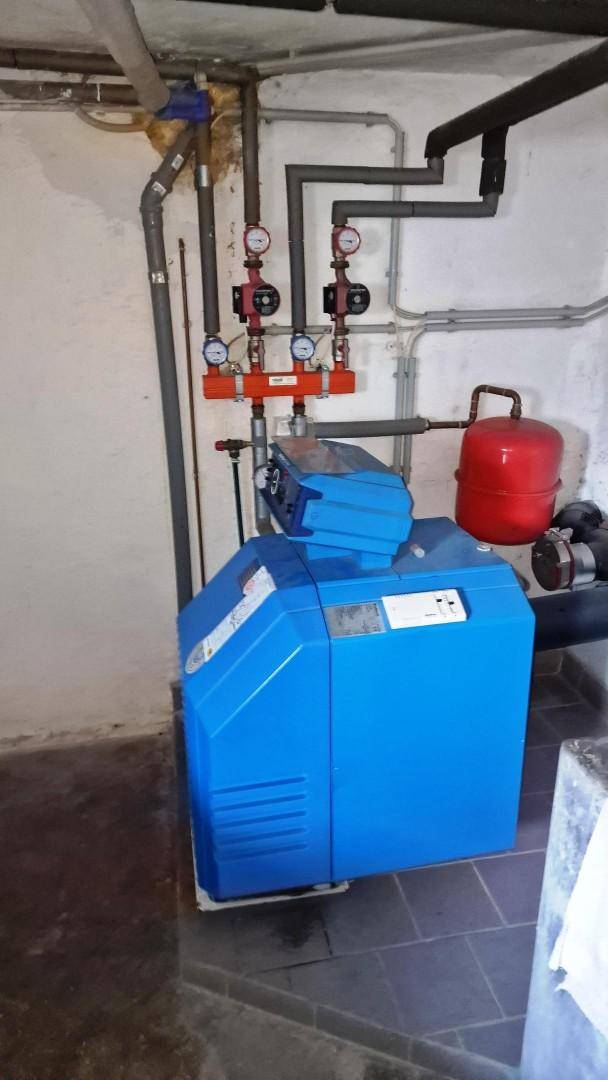 Heizungsanlage mit blauer Einheit und sichtbaren Rohren in einem Technikraum.