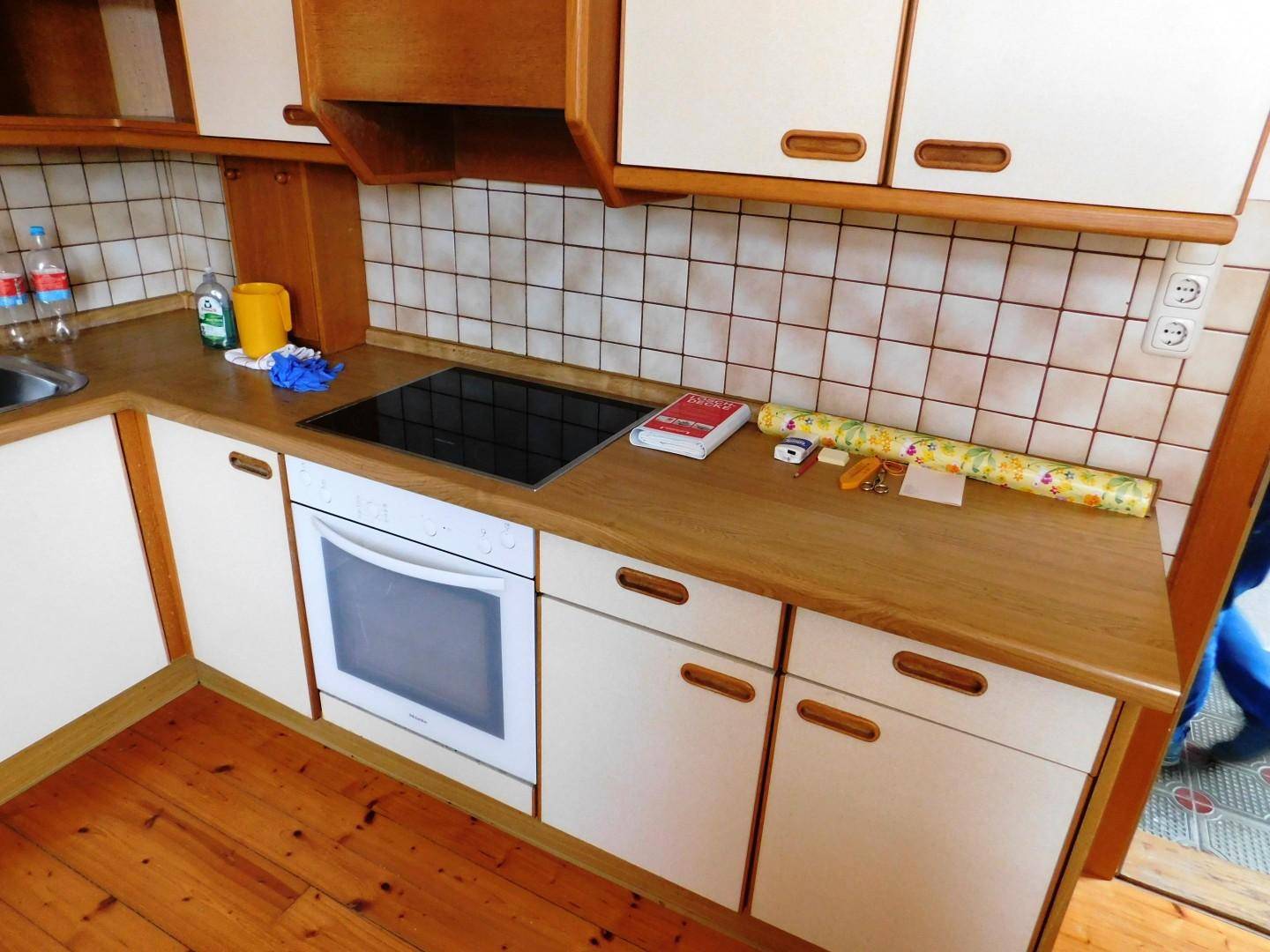Funktionale Küche mit hellen Holzschränken, weißer Arbeitsplatte und integriertem Kochfeld und Backofen.