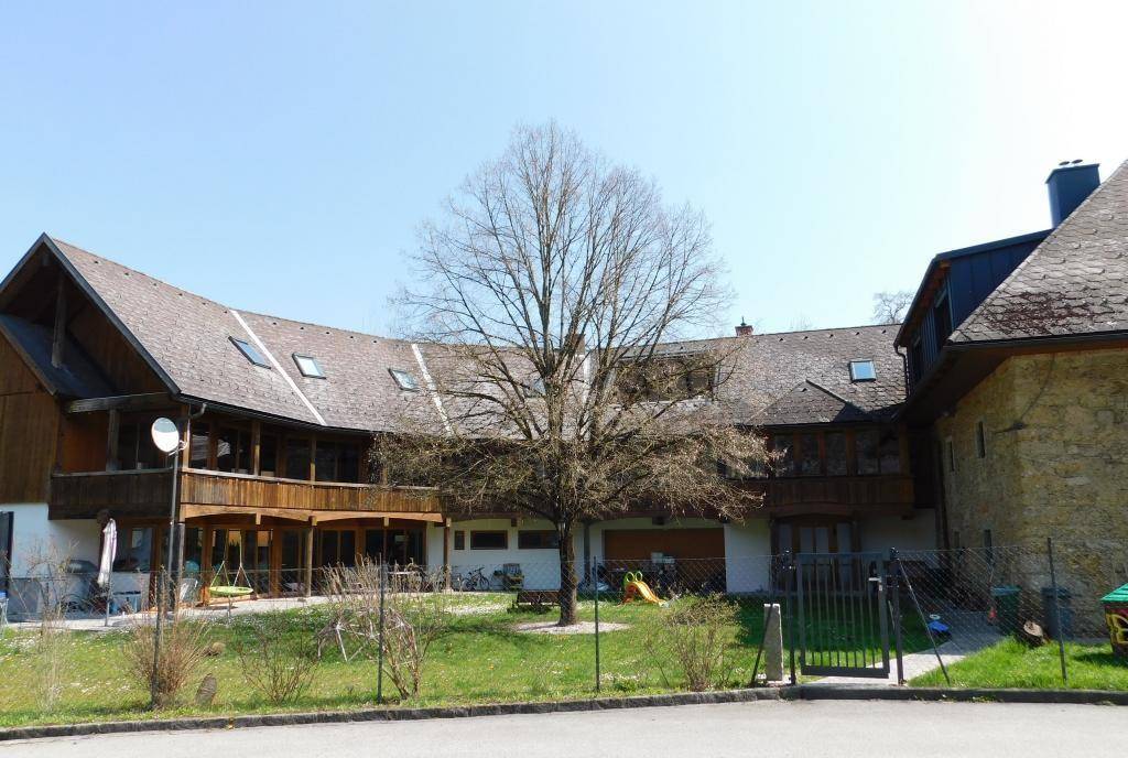 Gesamtansicht des weitläufigen Anwesens von der Straße, mit Hauptgebäude und langem Anbau mit Balkon.