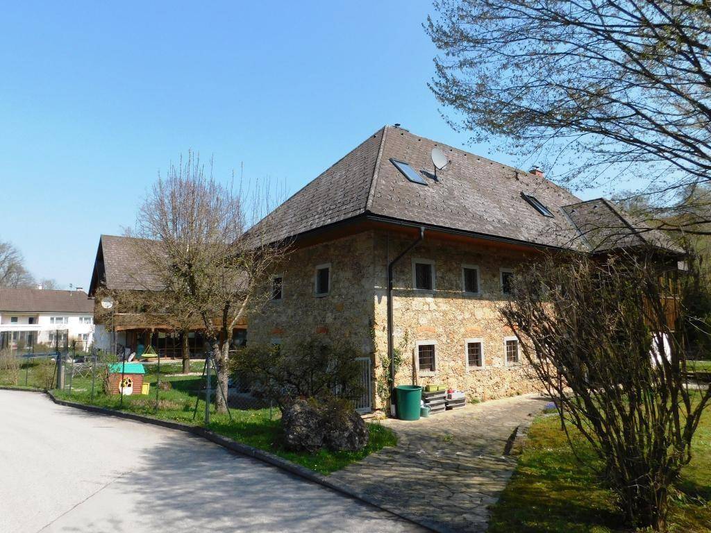 Seitenansicht des Hauses mit rustikaler Steinfassade und einem gepflasterten Zugangsbereich.