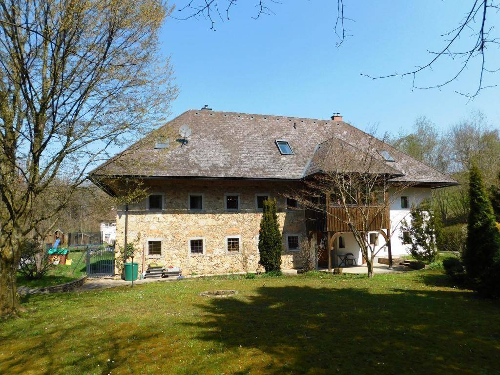 Großzügiger Garten mit Rasenfläche und altem Baumbestand vor der beeindruckenden Steinfassade des Anwesens.