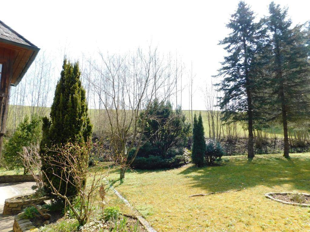 Gepflegter Gartenbereich mit vielfältiger Bepflanzung und Blick auf die umliegende grüne Hügellandschaft.