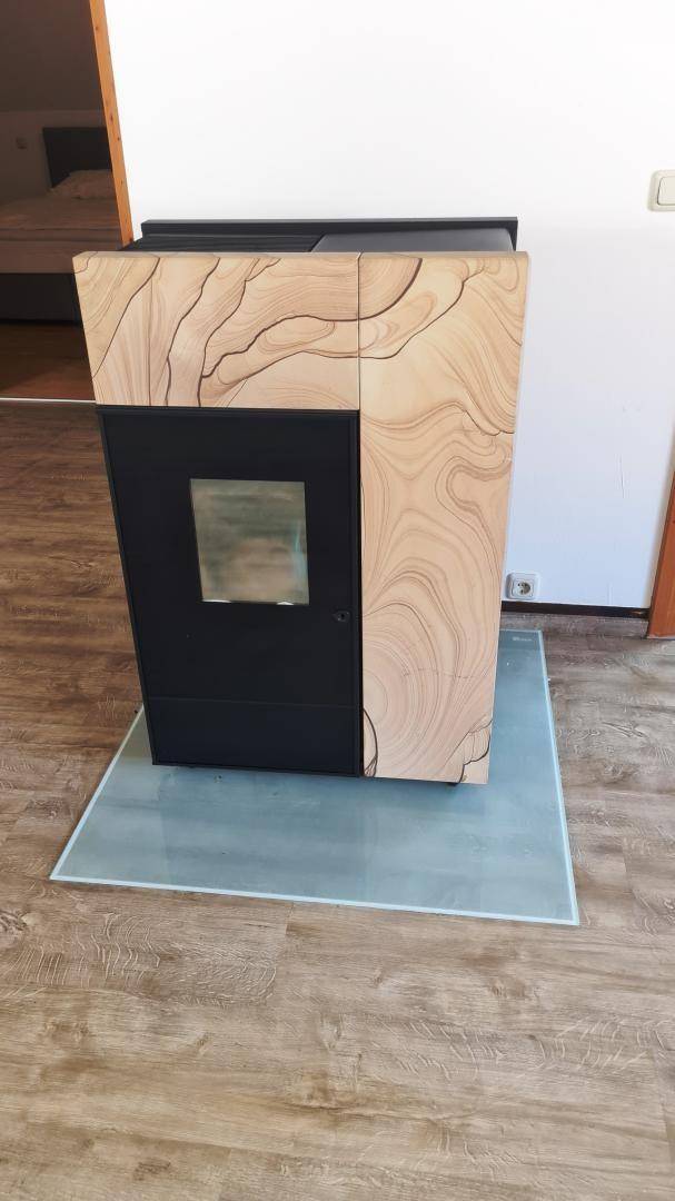 Moderner Holzofen mit dekorativer Steinverkleidung auf einer Glasplatte im Wohnbereich.