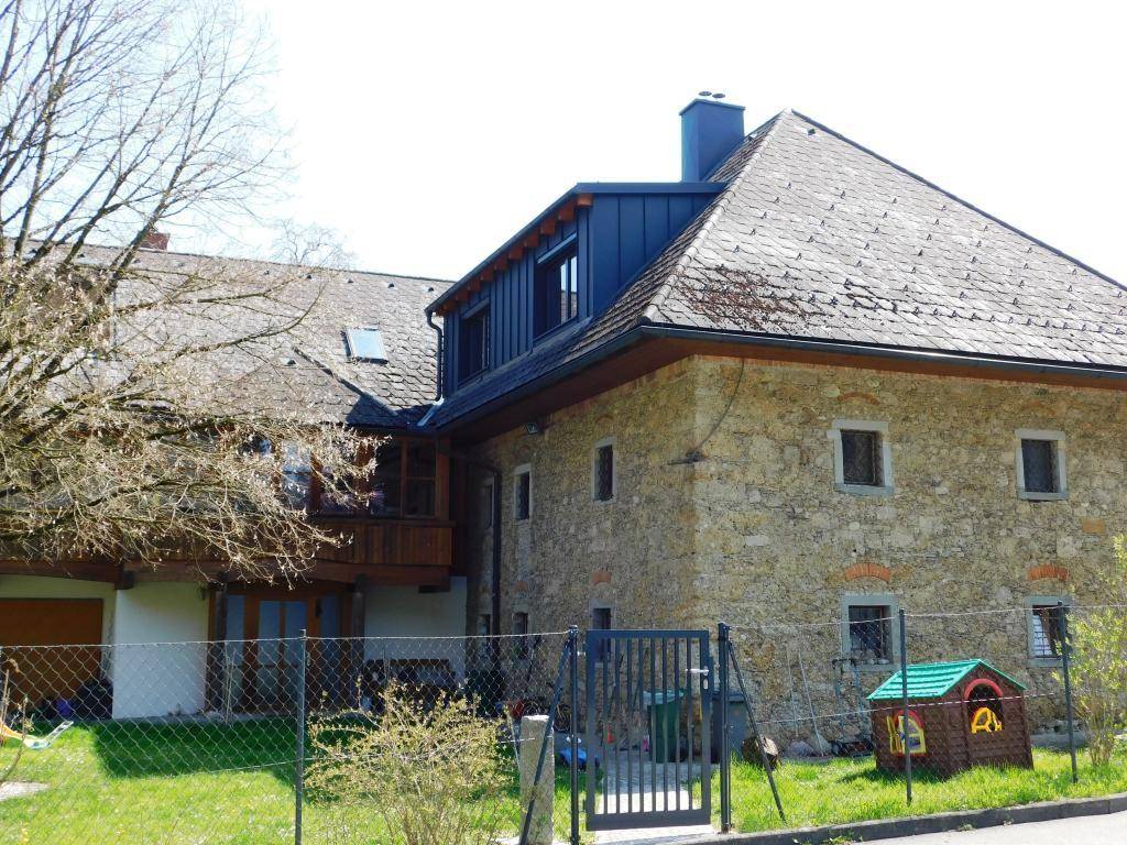 Nahaufnahme der Steinfassade mit modernem Dachausbau und Gaube, die das historische Gebäude ergänzt.