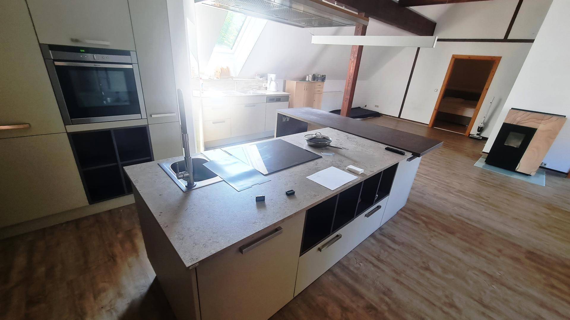 Moderne Küche mit Kochinsel, integriertem Backofen und Induktionskochfeld unter einem Dachfenster.