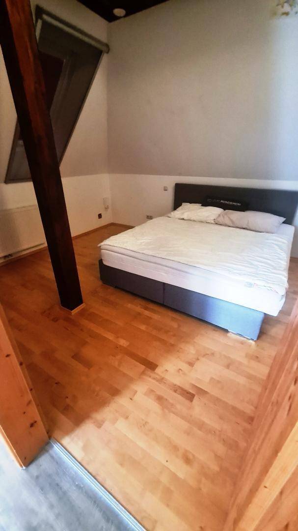 Gemütliches Schlafzimmer mit Doppelbett, Holzboden und schrägen Wänden unter einem Dachfenster.