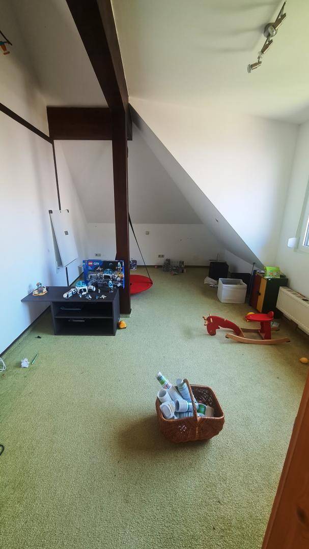 Kinderzimmer mit grünem Teppichboden, Spielzeug und schrägen Wänden unter dem Dach.