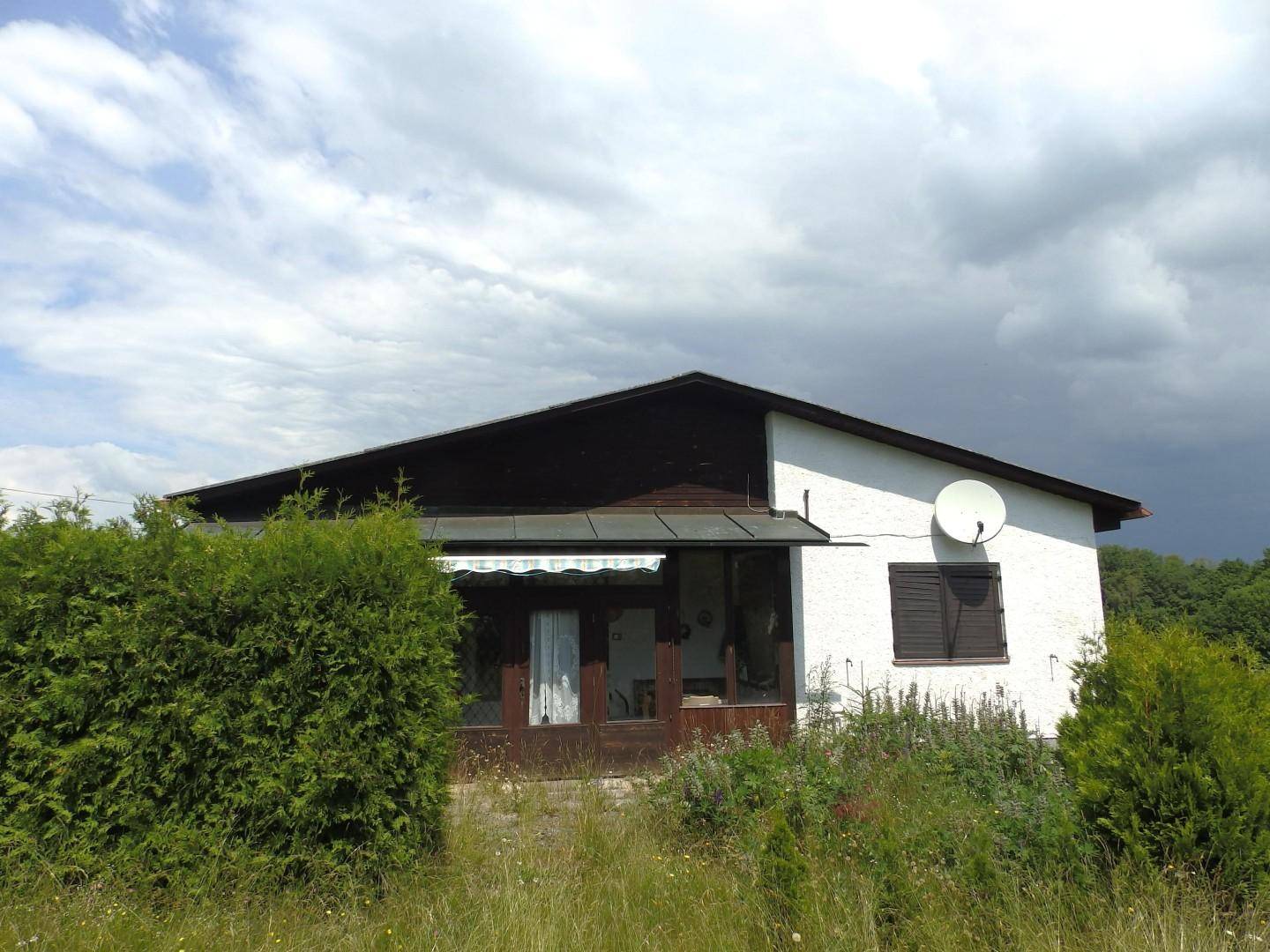 Hausansicht mit verglastem Anbau und Markise unter einem bewölkten Himmel.