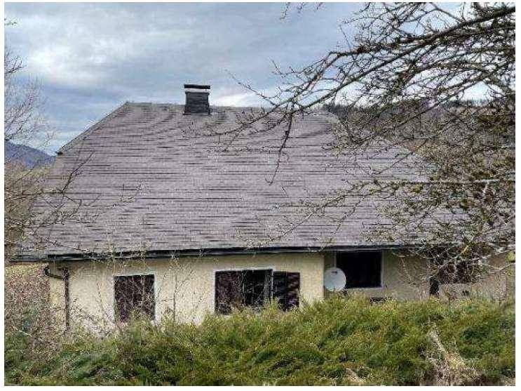 Nahaufnahme des Daches und der Fassade eines Landhauses mit Satellitenschüssel und Hecke.