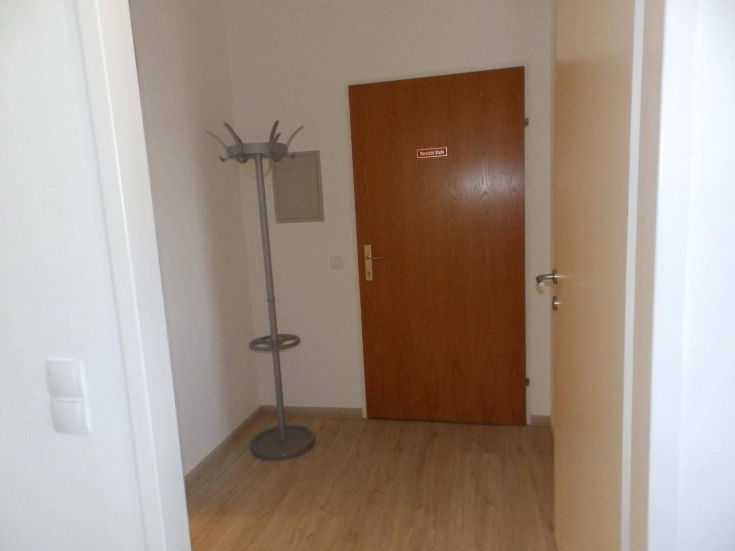Eingangsbereich mit Garderobenständer und einer Holztür, die zu weiteren Räumen führt.