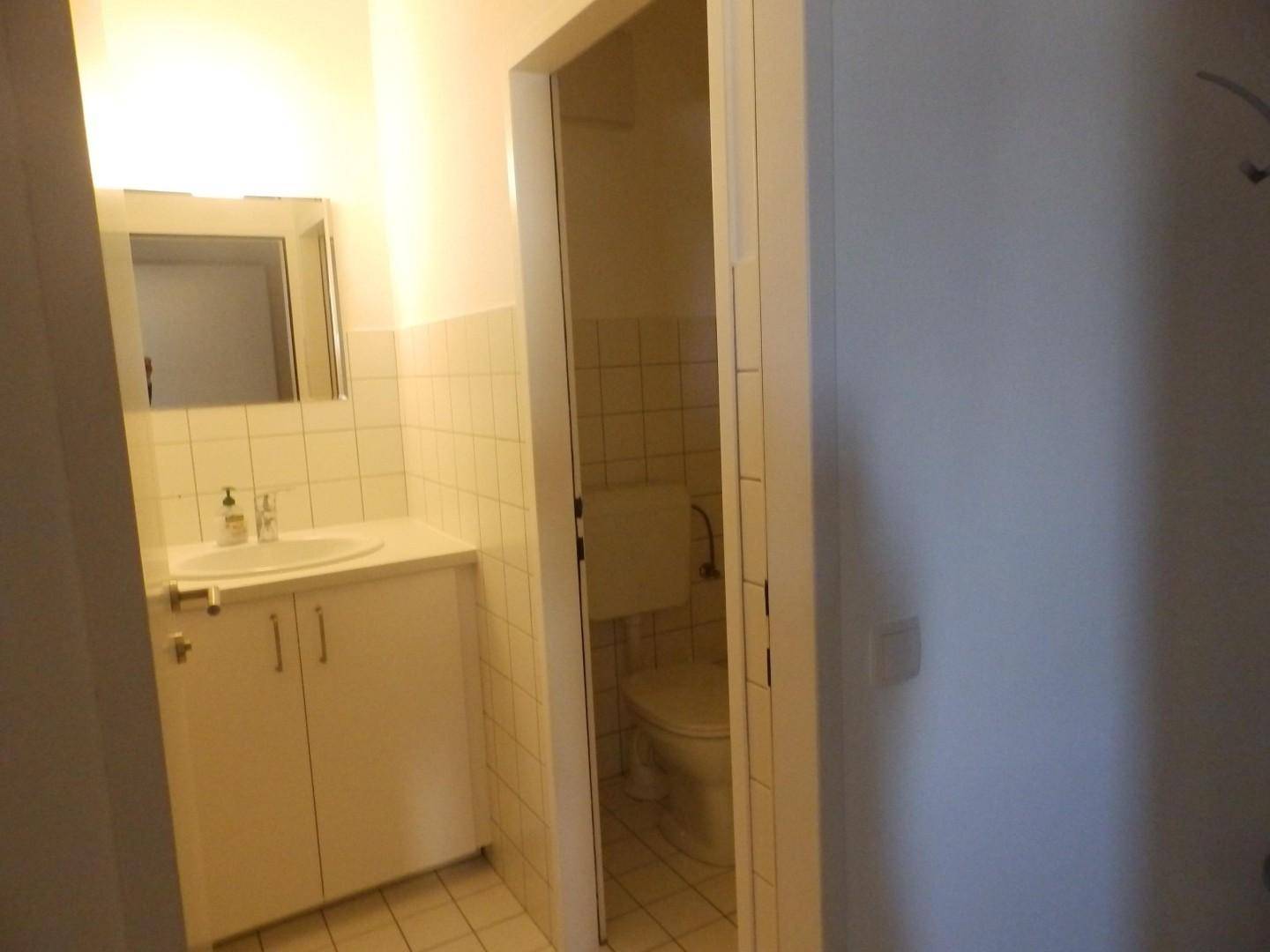 Badezimmer mit Waschbecken, Spiegelschrank und Blick in einen separaten Toilettenraum.