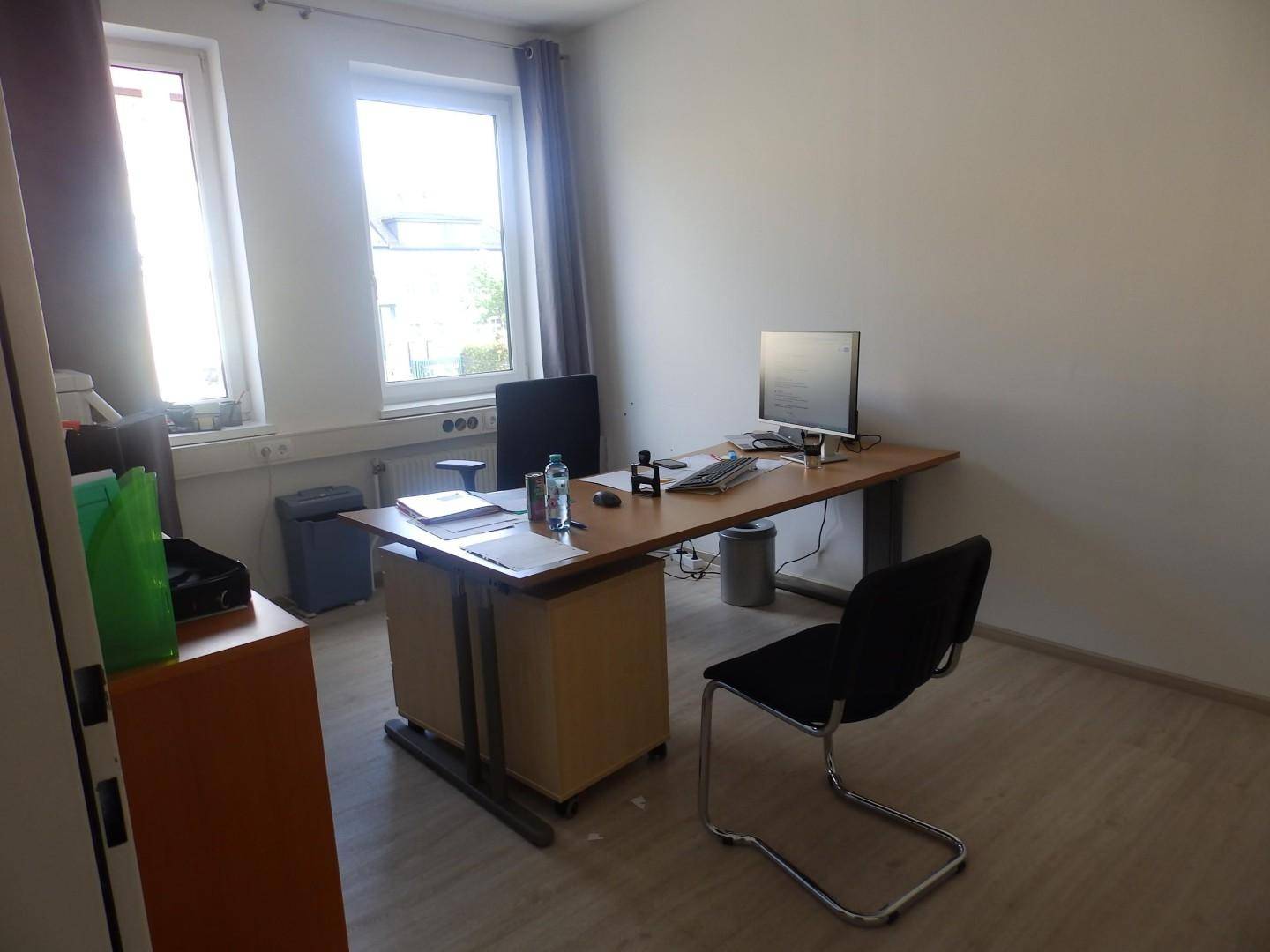 Einzelbüro mit Schreibtisch, Bürostuhl und zwei Fenstern für ausreichend Tageslicht.