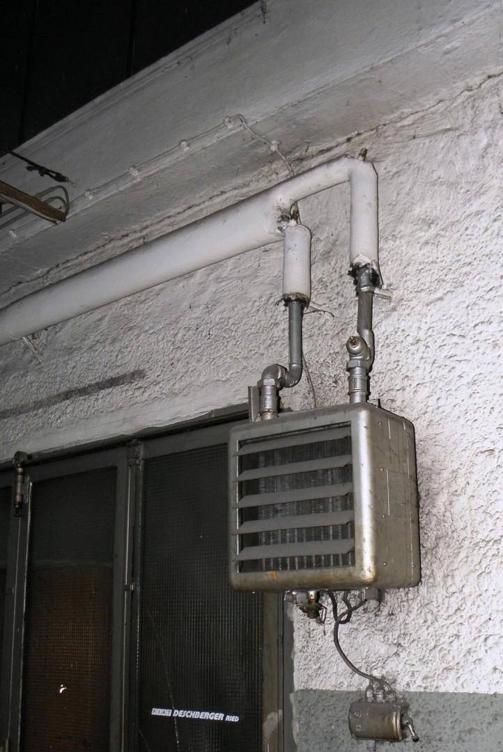 Detailansicht eines alten Heizkörpers und Rohrsystems an einer rauen Wand.