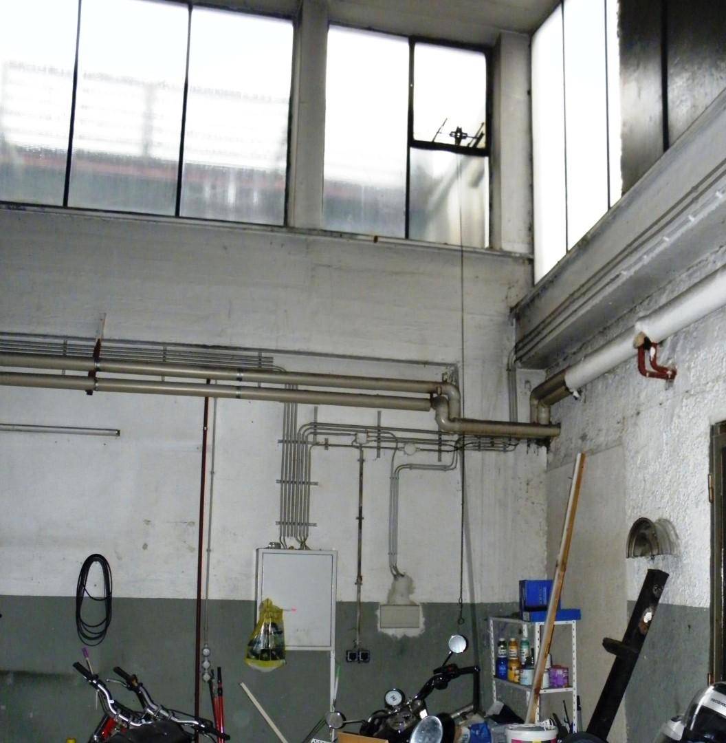 Innenansicht eines Raumes mit sichtbaren Rohren, hohen Fenstern und industriellem Charakter.